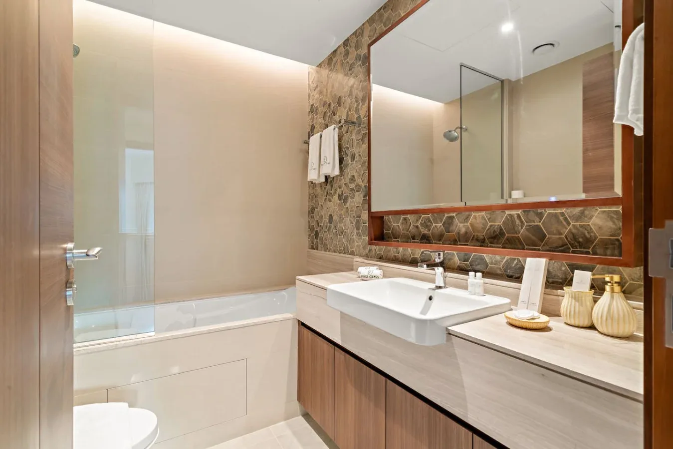 A bright bathroom with a bathtub, glass shower screen, and wide vanity.