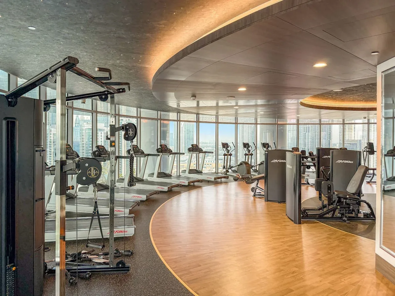A fitness room with exercise machines and treadmills beside large windows.