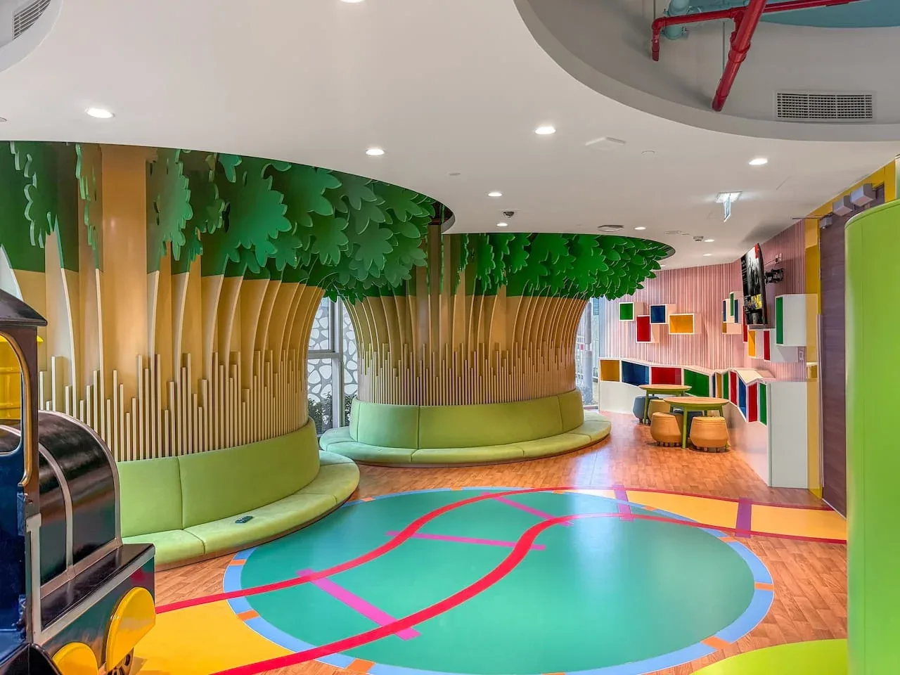 A colorful indoor play area features curved green seating and a bright patterned floor.