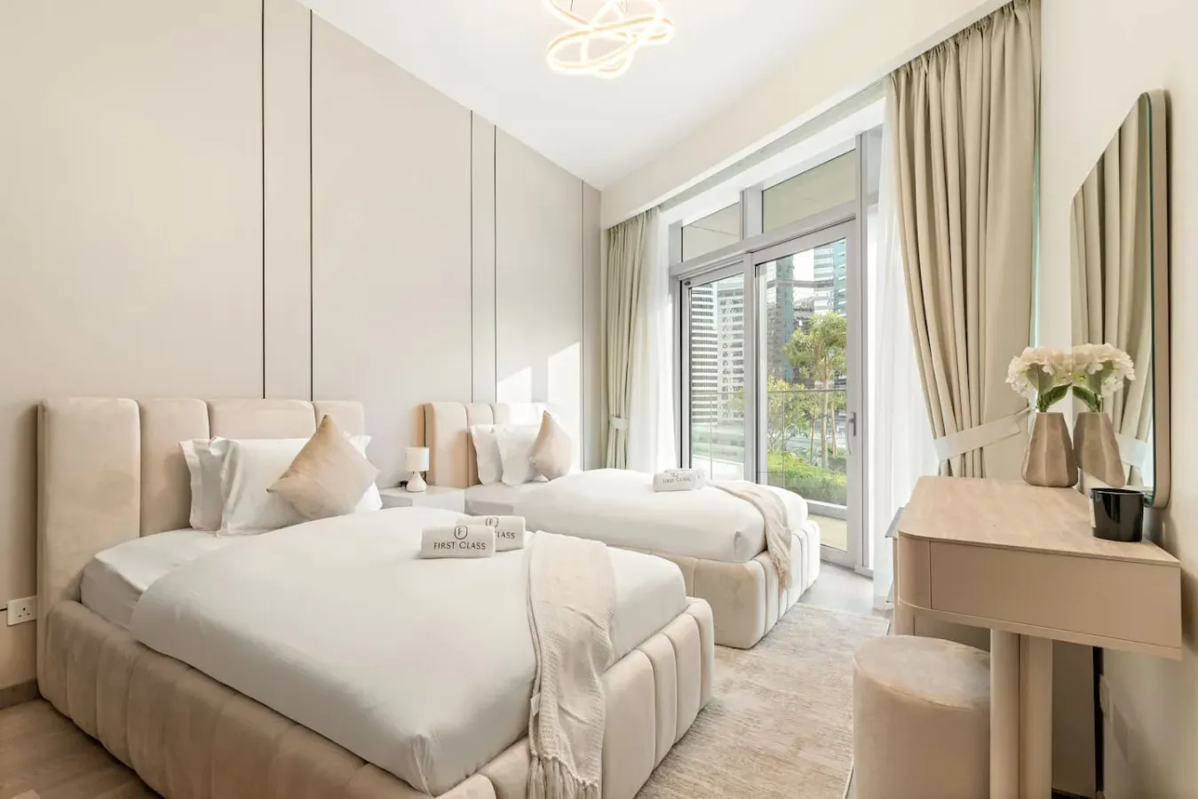 A bright bedroom with two beds, tall windows, and neutral decor.