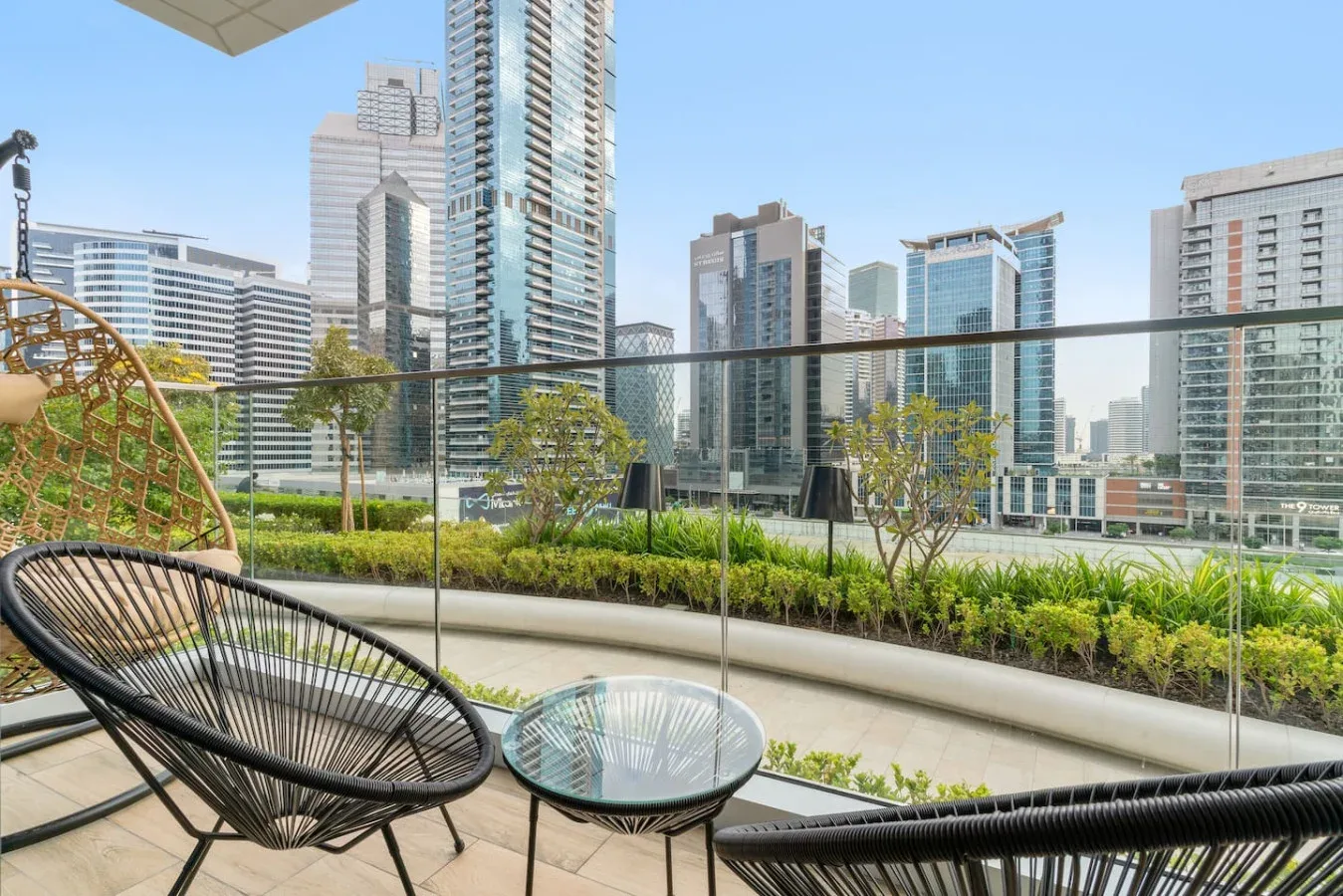 A rooftop terrace has outdoor seating and a glass railing overlooking city buildings.