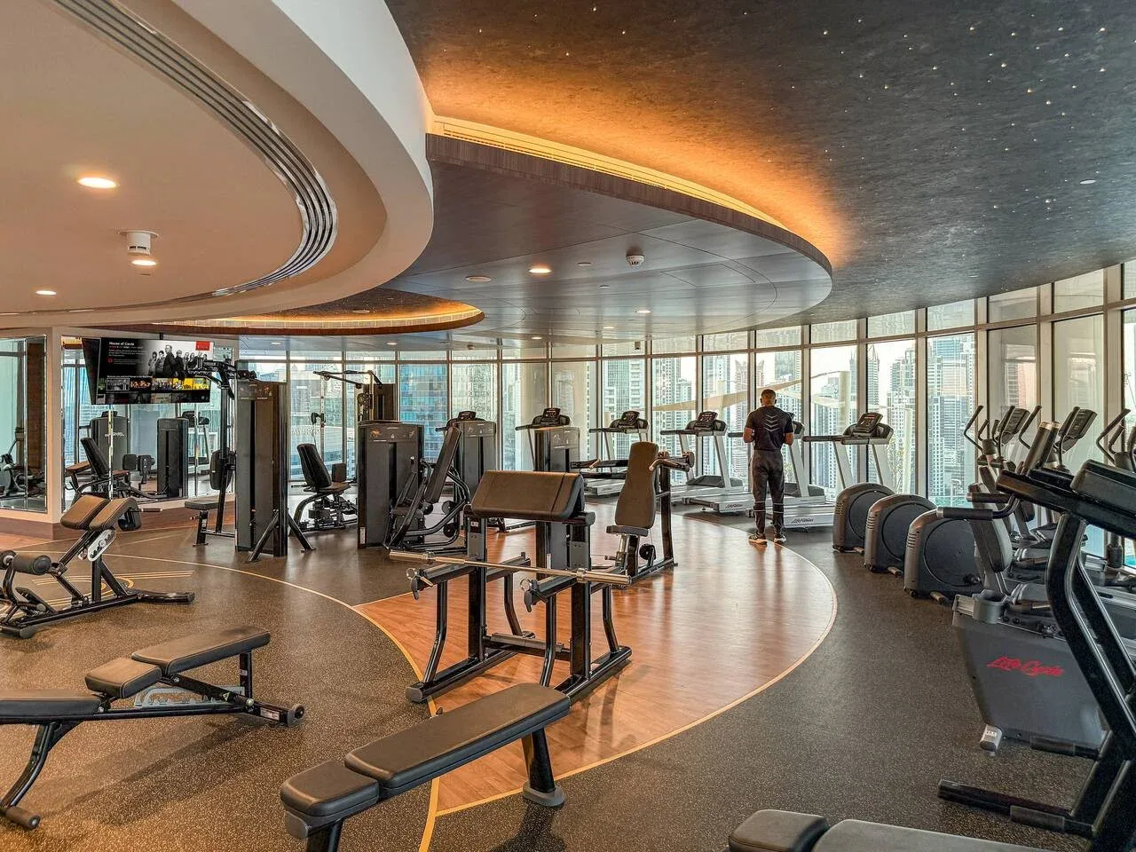 A spacious gym with exercise machines and floor-to-ceiling windows.