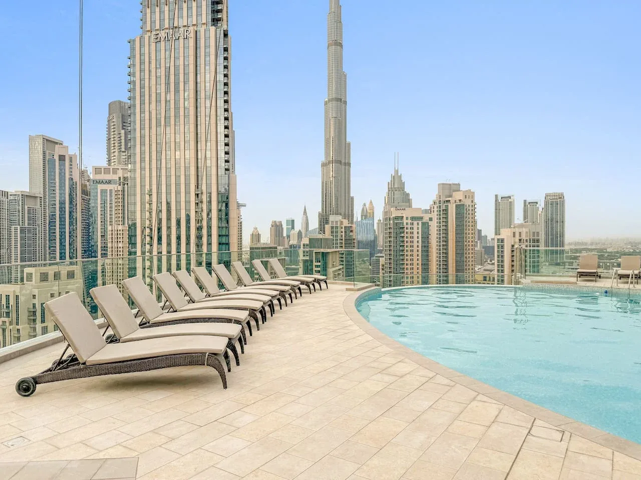 A rooftop swimming pool and lounge seating overlook a skyline of tall buildings.