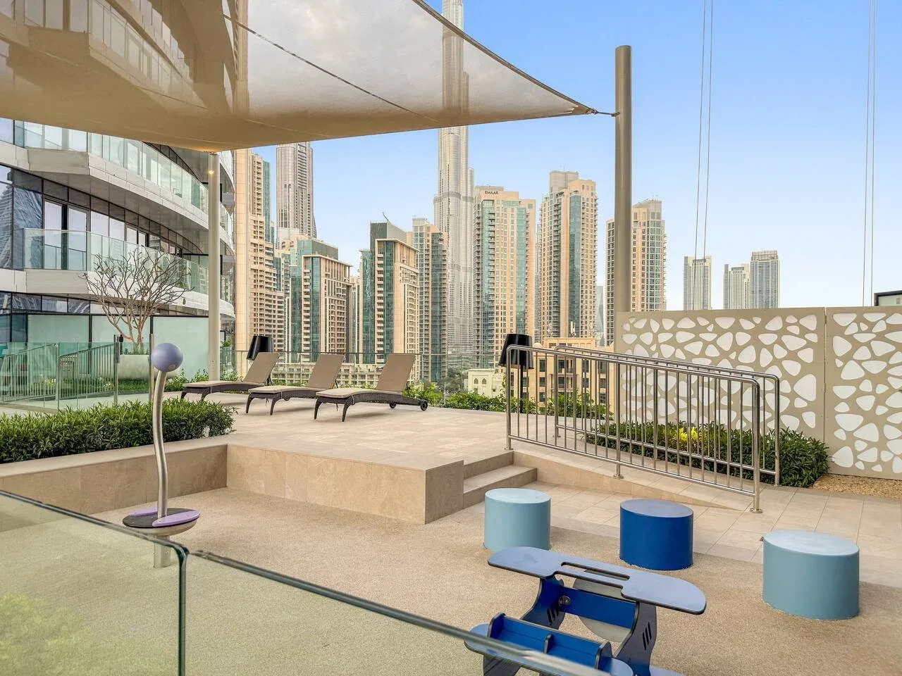 A rooftop terrace with lounge seating, shade canopy, and city buildings in view.
