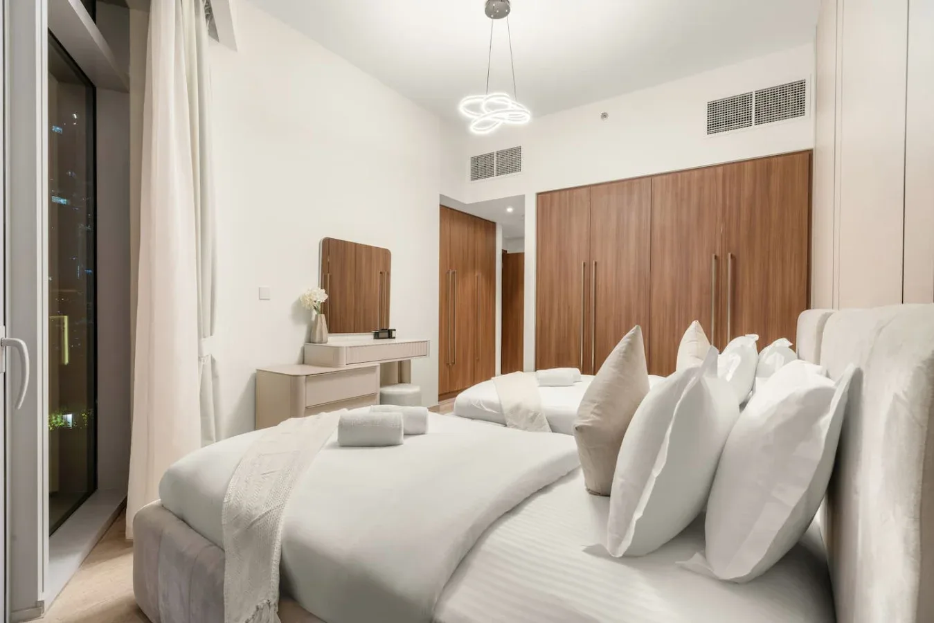 A bright bedroom with neatly arranged beds and a small dressing table.