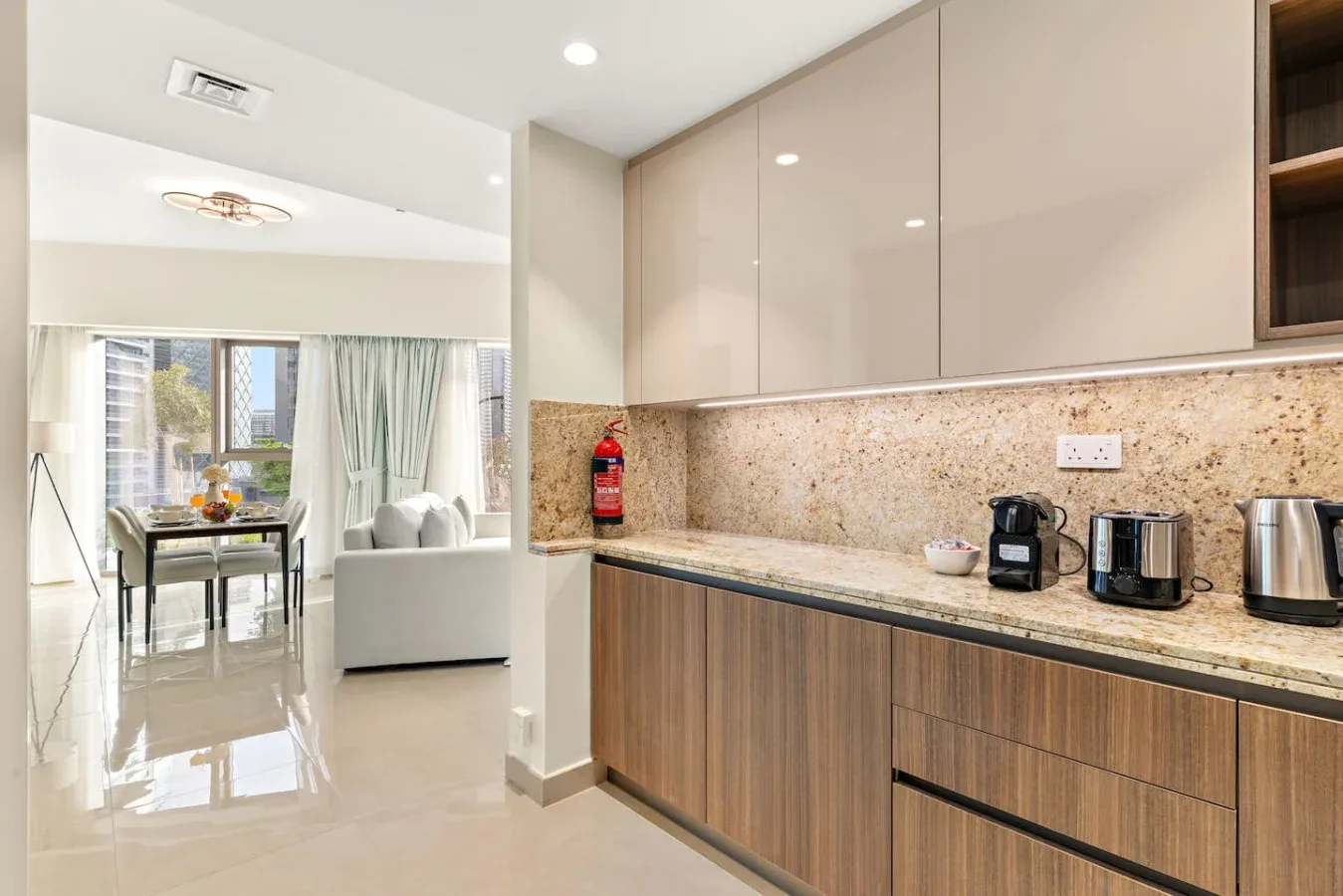 A modern kitchen counter with small appliances opens onto a bright dining and living area.