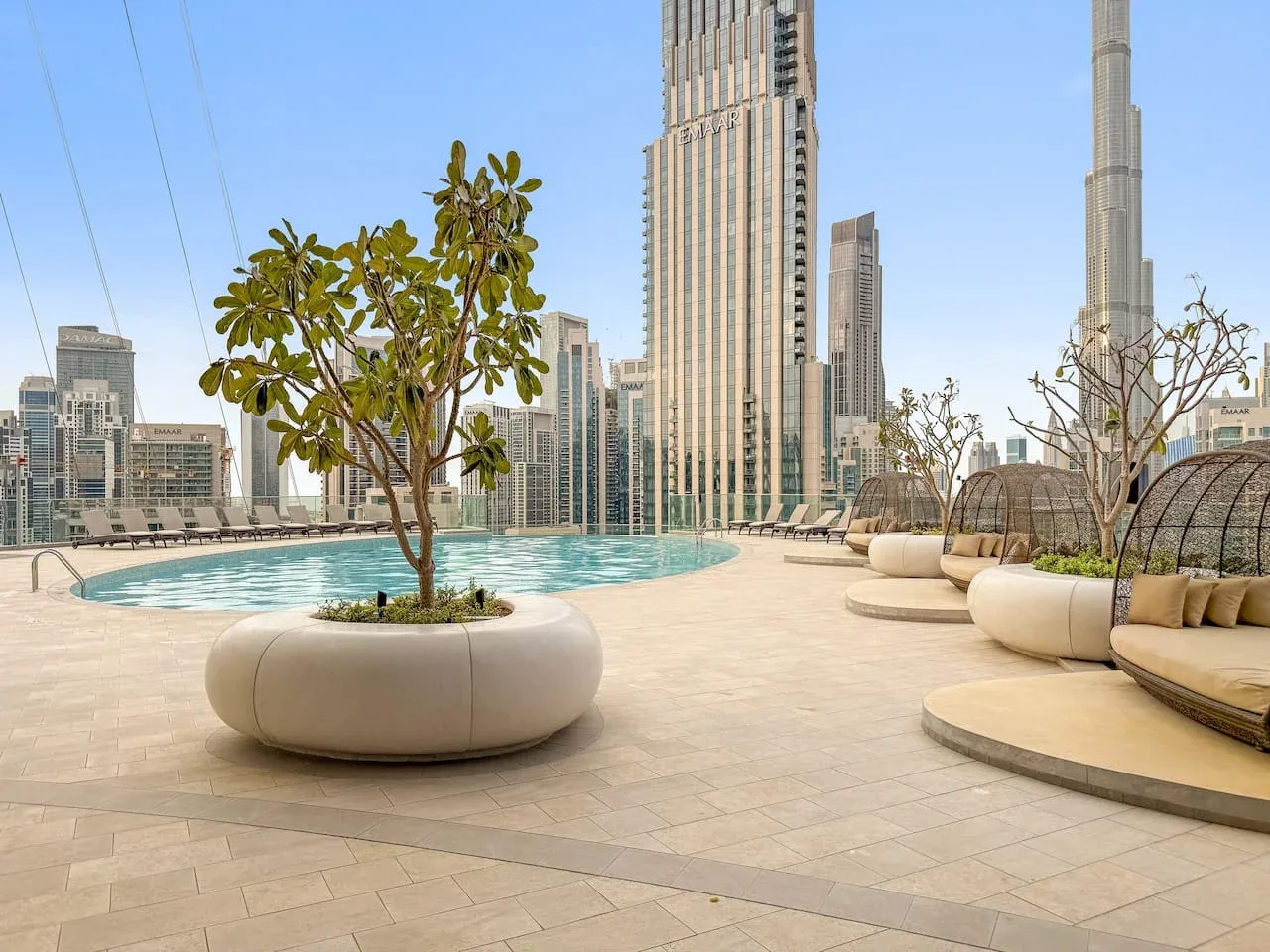 A rooftop terrace with a curved pool, planters, and city skyscrapers in the background.