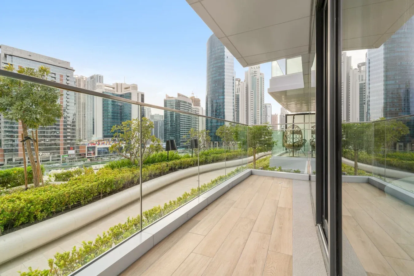 A balcony with glass railing and planters overlooks a cluster of modern city buildings.