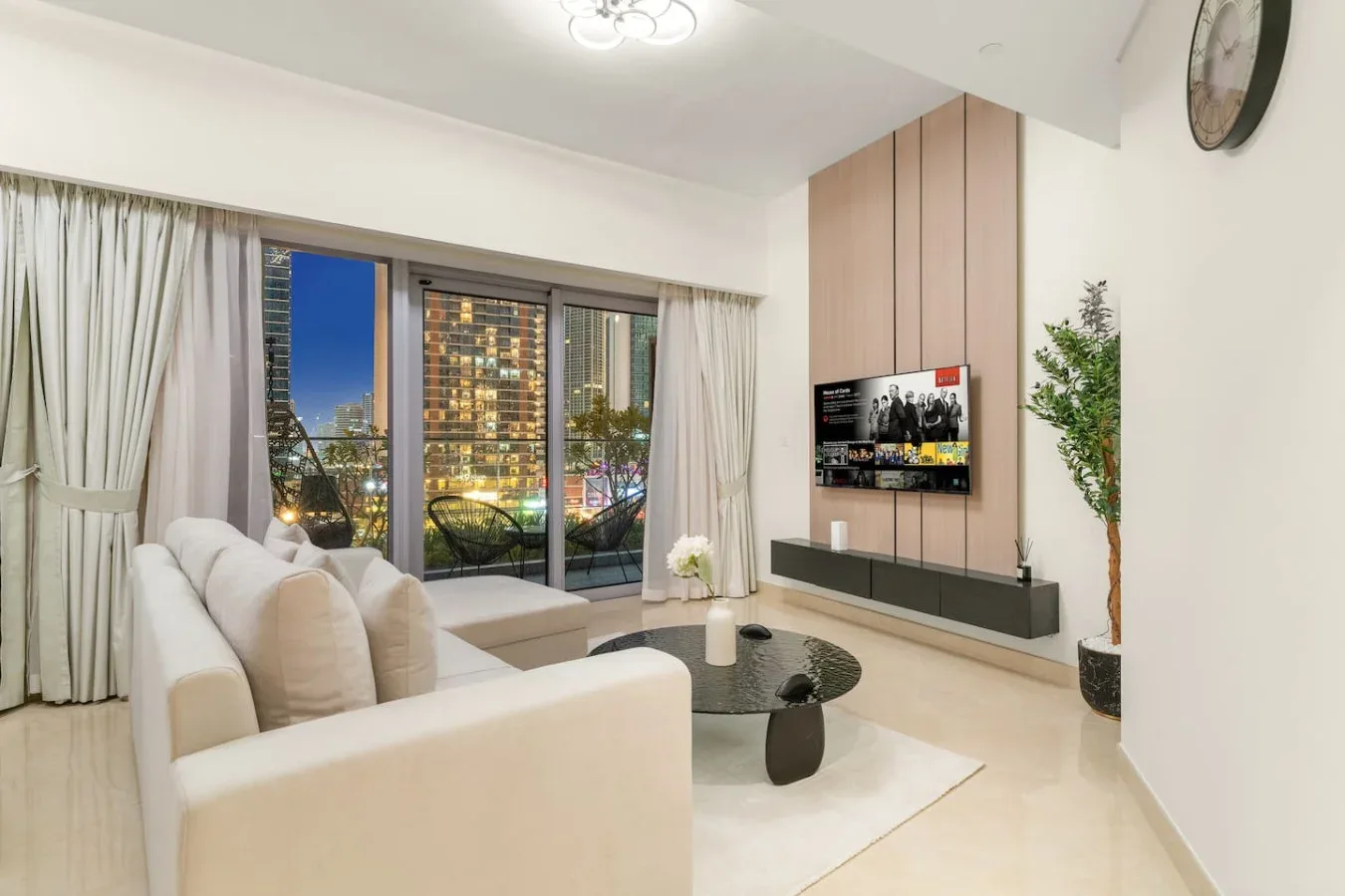 A bright living room with seating, a coffee table, and a city view through large windows.