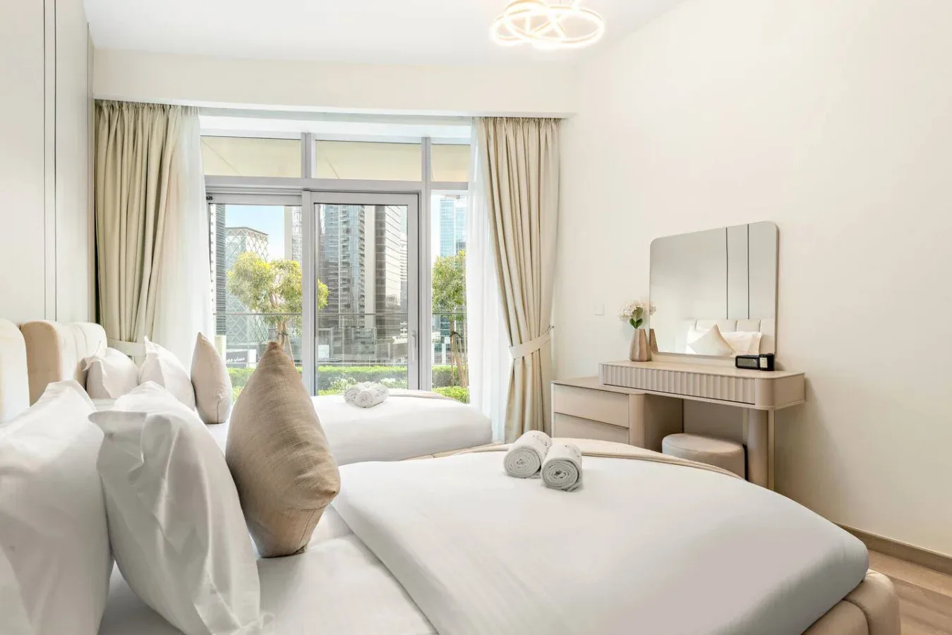 A bright bedroom with a large bed facing a window and city buildings.