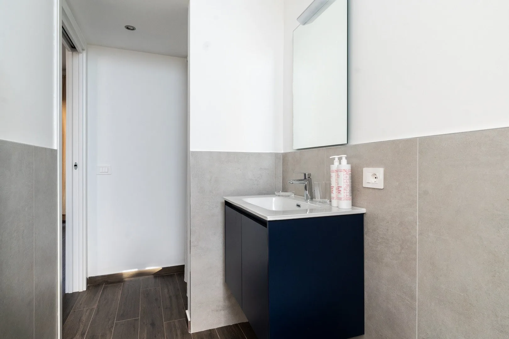 Un lavabo de baño con espejo junto a una puerta abierta.