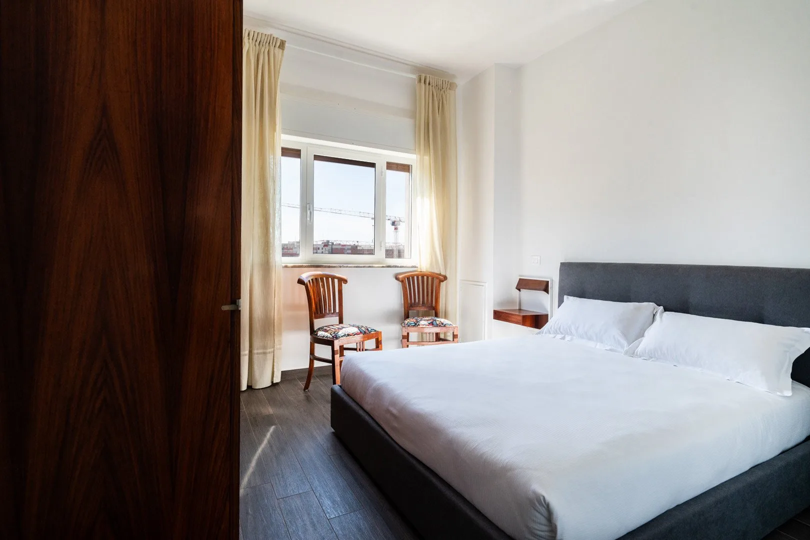 Un dormitorio luminoso con una cama grande y una ventana enmarcada por cortinas.
