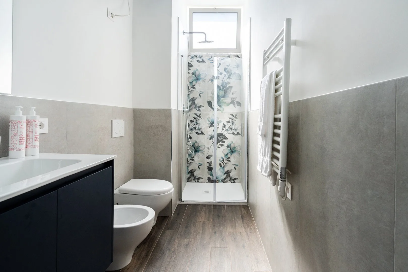 Un baño con una ducha de vidrio y un panel con motivos de hojas.