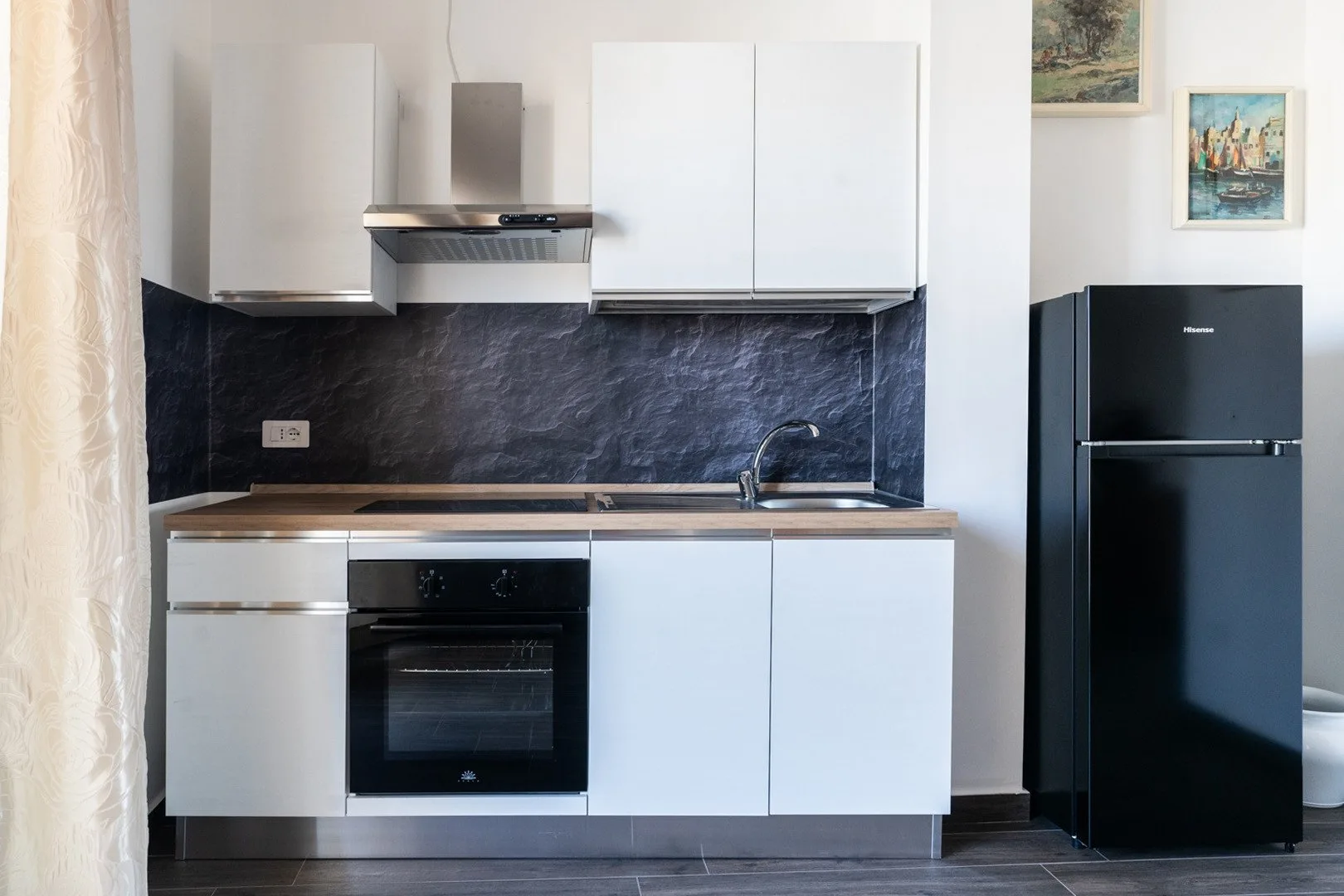 Una cocina moderna con gabinetes blancos, salpicadero oscuro y refrigerador negro.