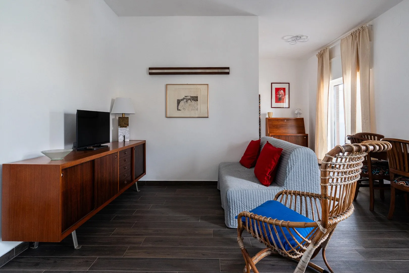 Una sala de estar con televisor, asientos y ventanas altas con cortinas.