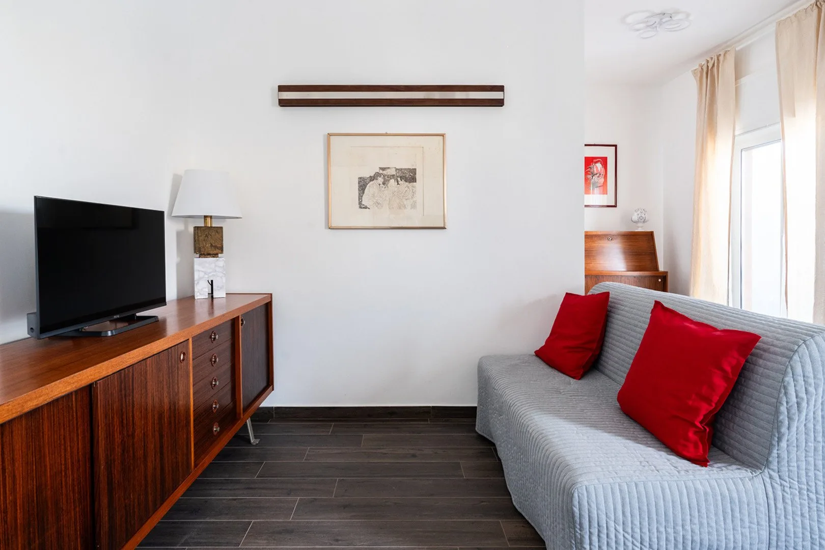 Una sala luminosa con un sofá gris y un televisor sobre un mueble de madera.