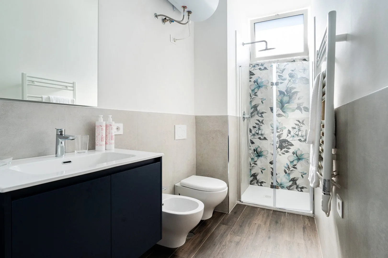 Un baño luminoso con un mueble oscuro y una ducha con paneles estampados de flores.