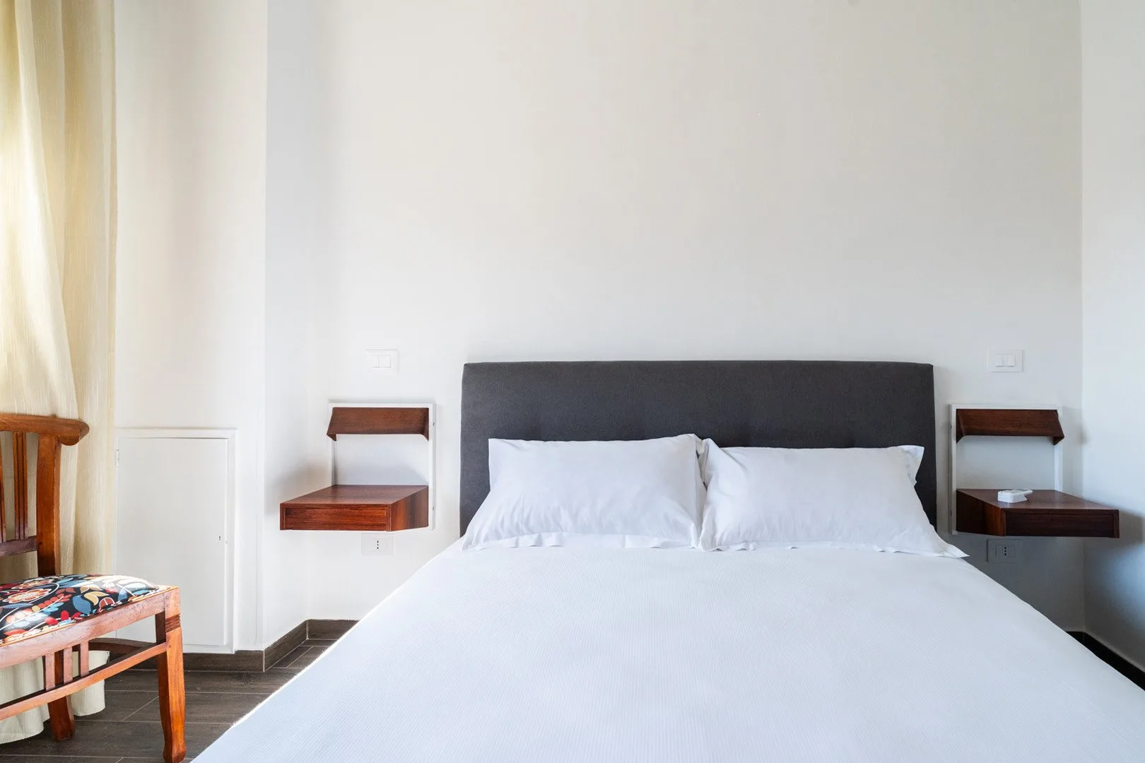 Un dormitorio con una cama blanca y un cabecero tapizado oscuro.