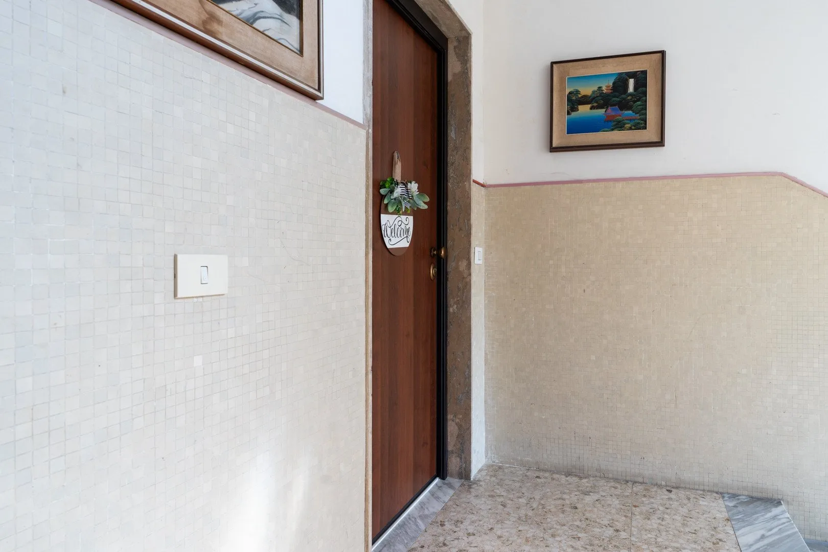 Un pasillo de azulejos con una puerta de madera y cuadros en la pared.