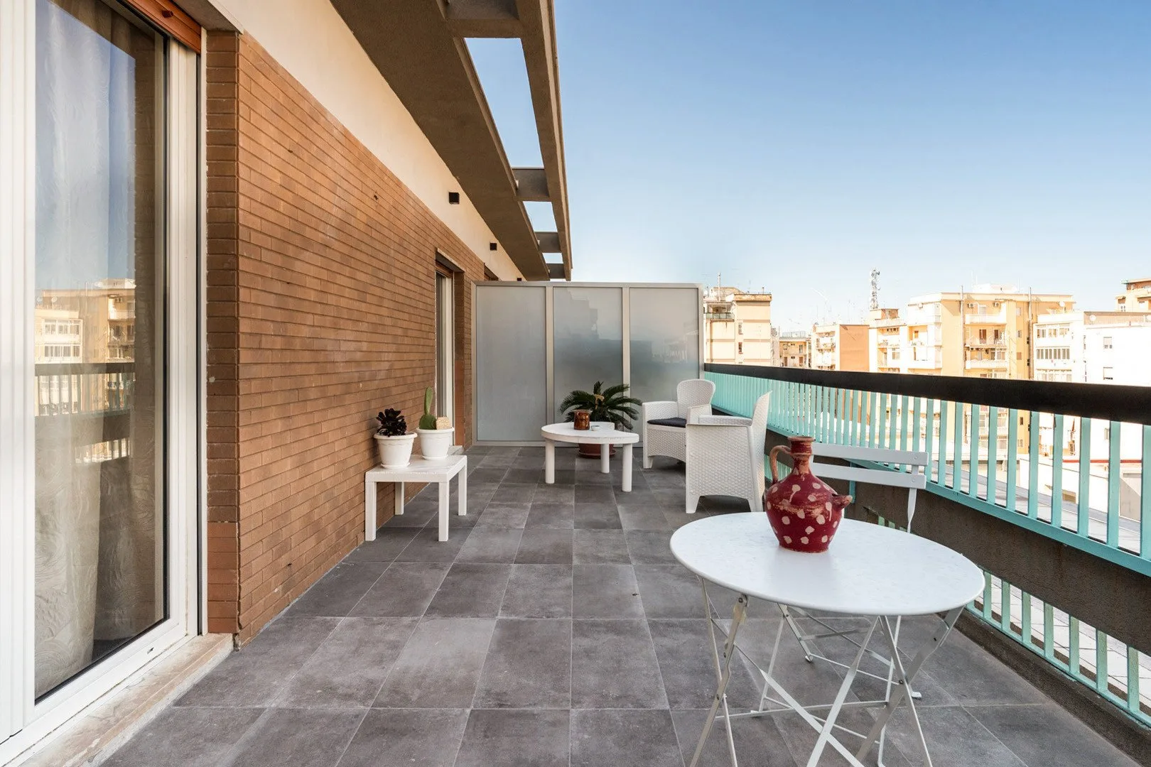 Un balcón amueblado con asientos al aire libre, una mesa y plantas en macetas.