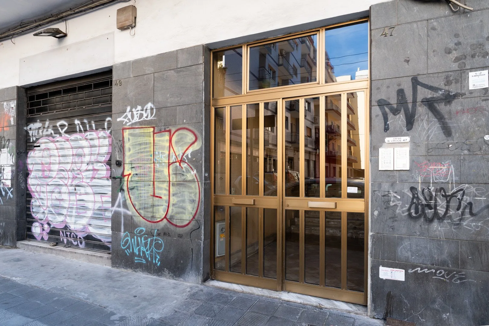 Una entrada de edificio a la calle, con una reja metálica y paredes con grafitis.