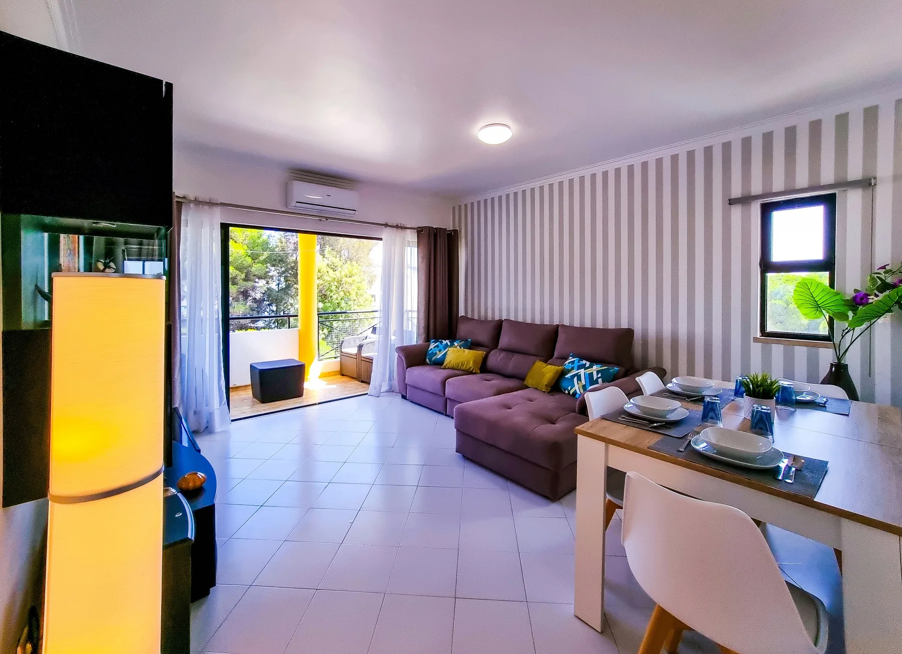 A living and dining area opens onto a balcony, with a sectional sofa and table.