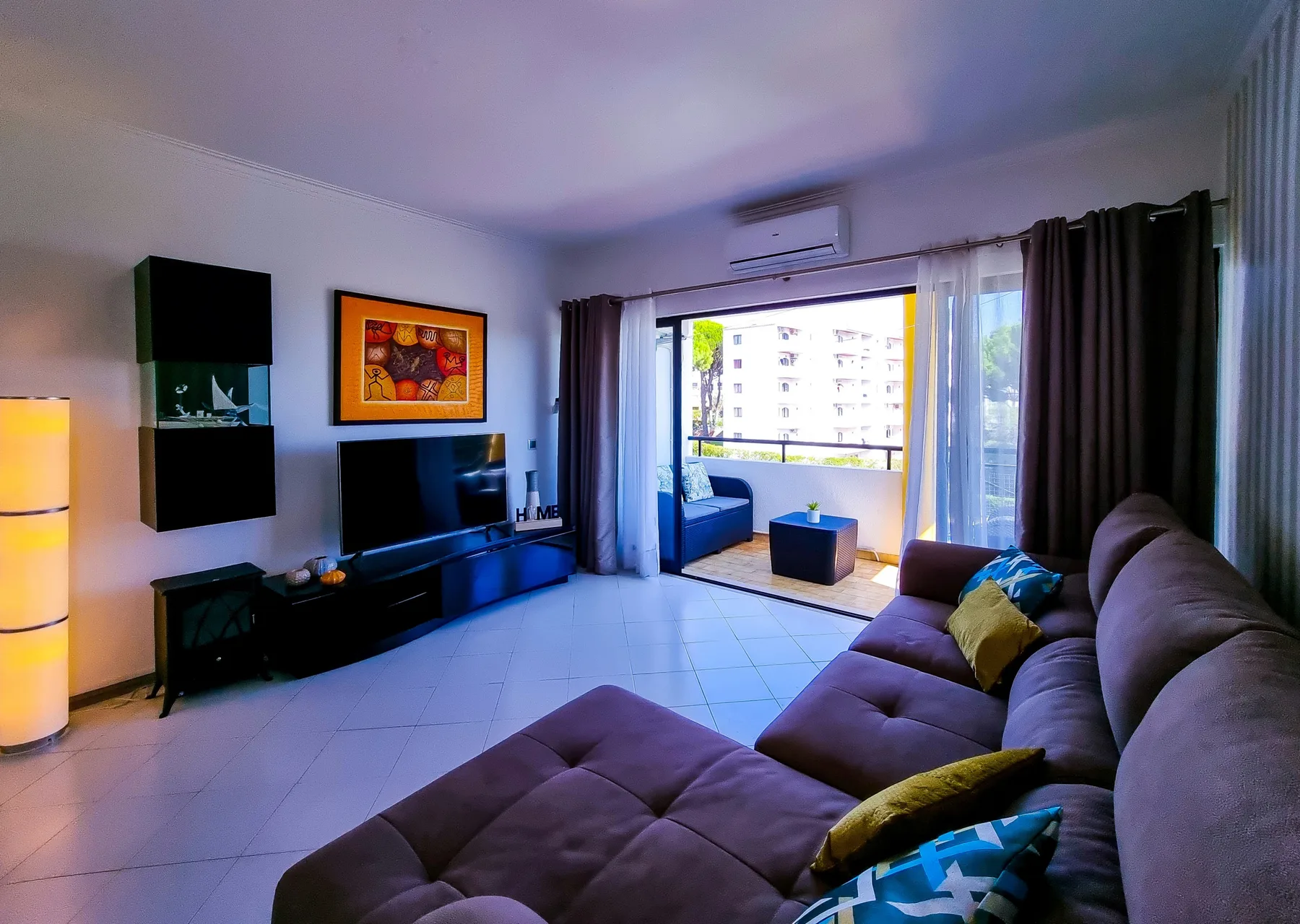 A living room with sectional seating and an open balcony overlooking nearby buildings.