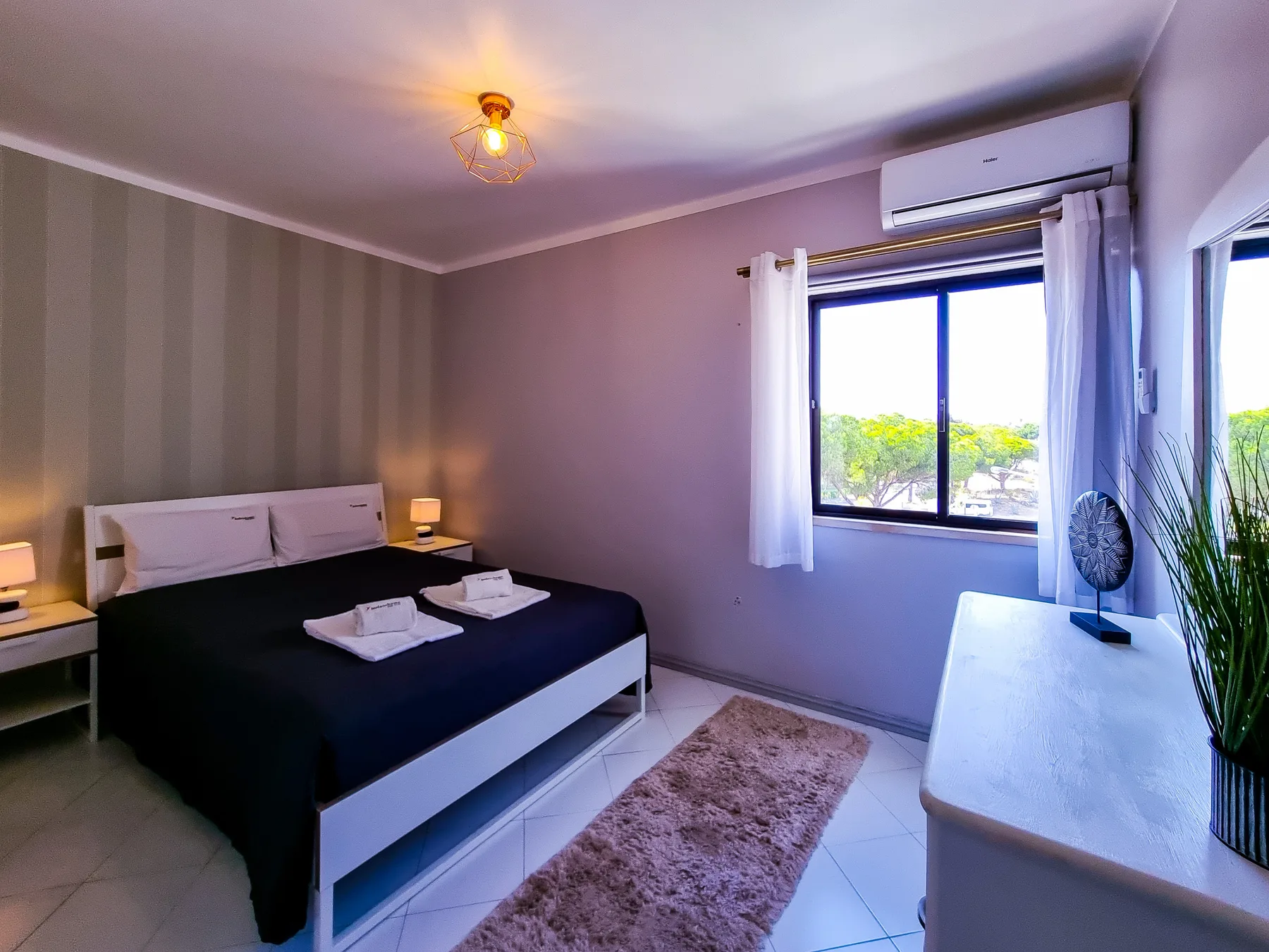 A bedroom with a double bed, bedside tables, and a window with curtains.