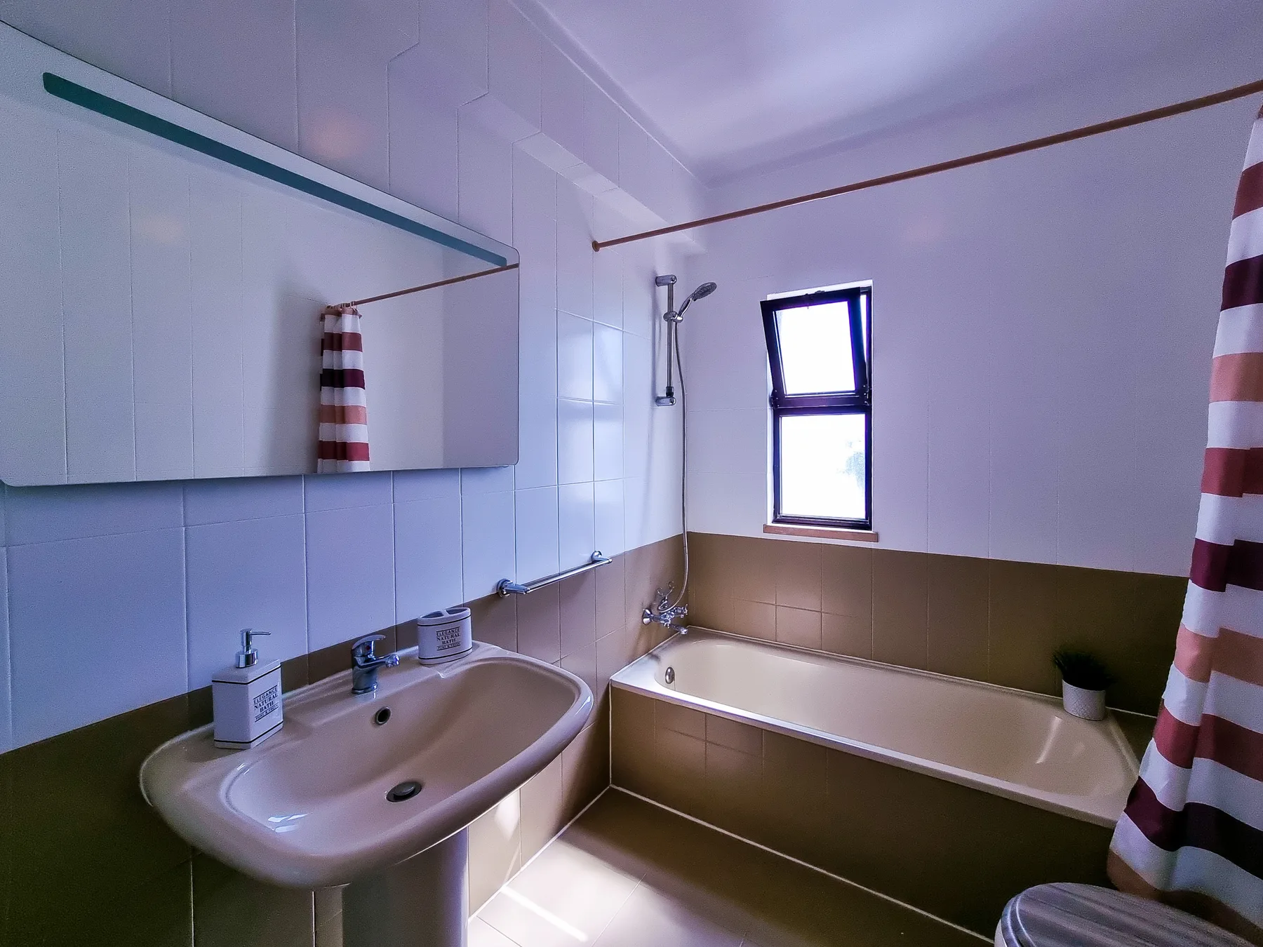 A tiled bathroom with a sink, bathtub, and striped shower curtain.