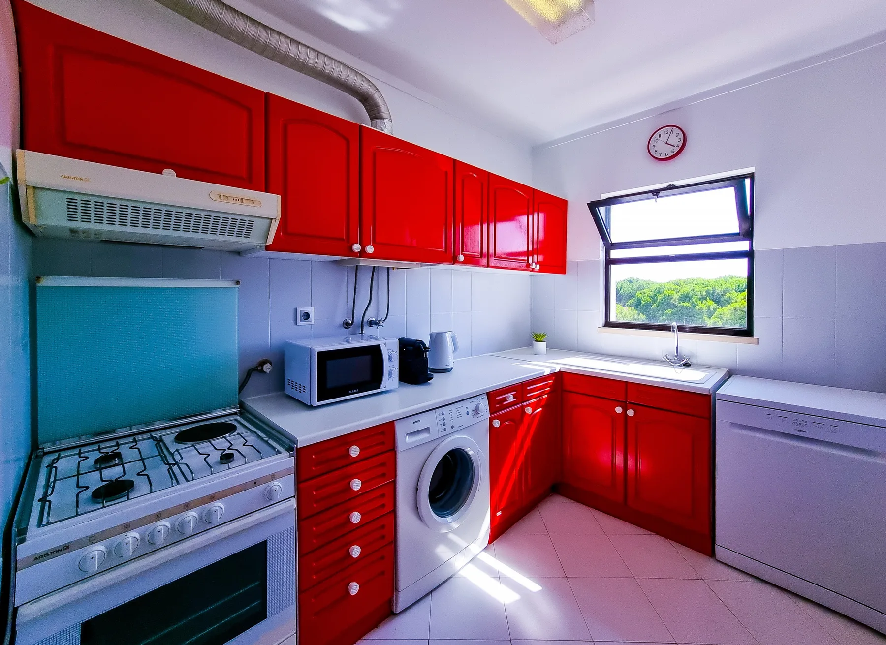 A bright kitchen with red cabinets, a stove, and a window overlooking greenery.