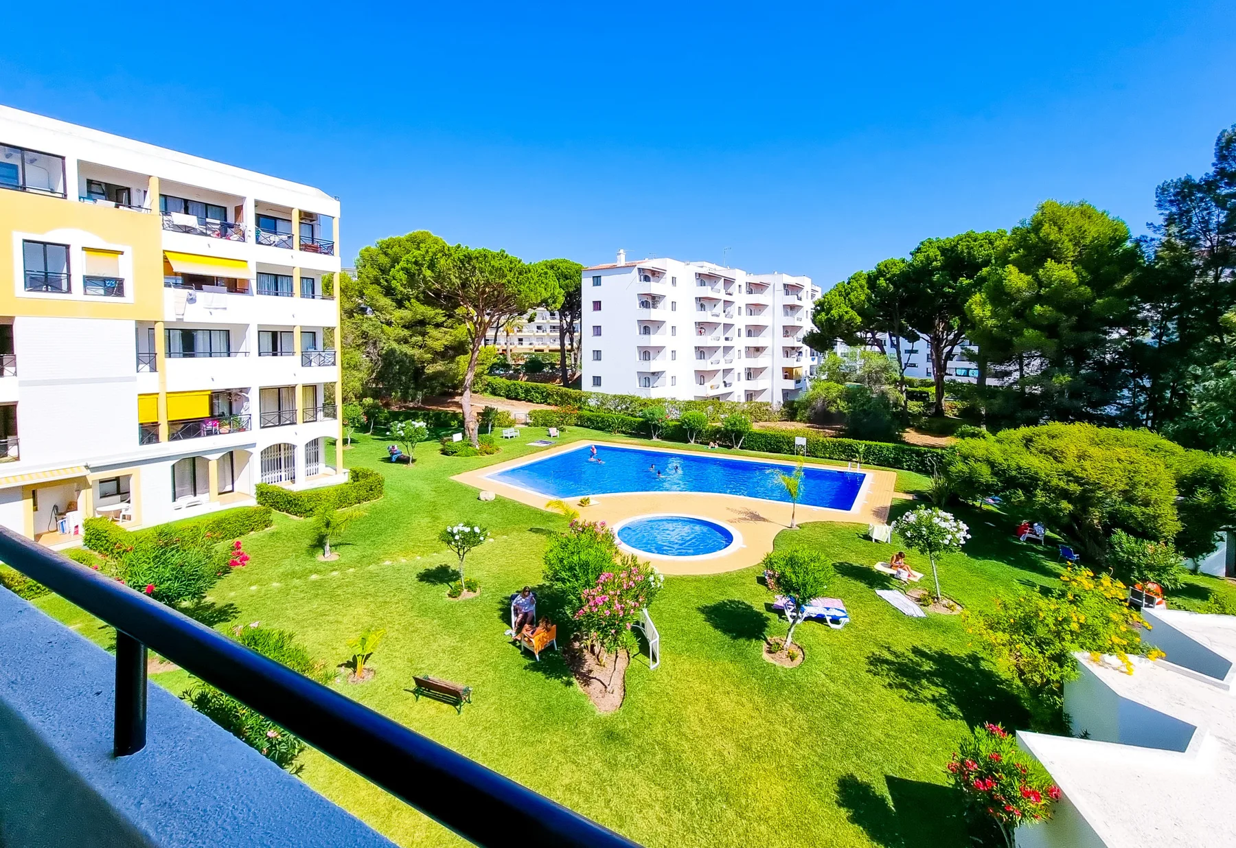 A balcony overlooks a swimming pool surrounded by landscaped grounds and apartment buildings.