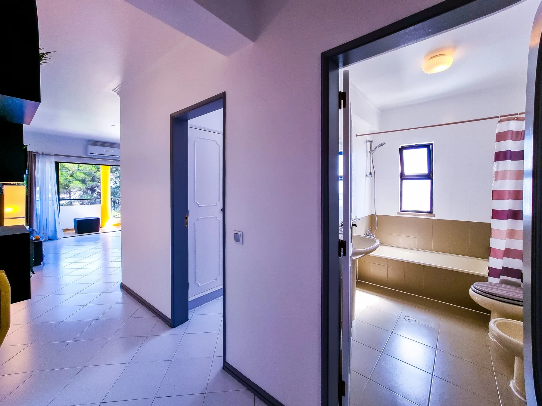 A tiled hallway opens onto a bathroom with a bathtub and shower.