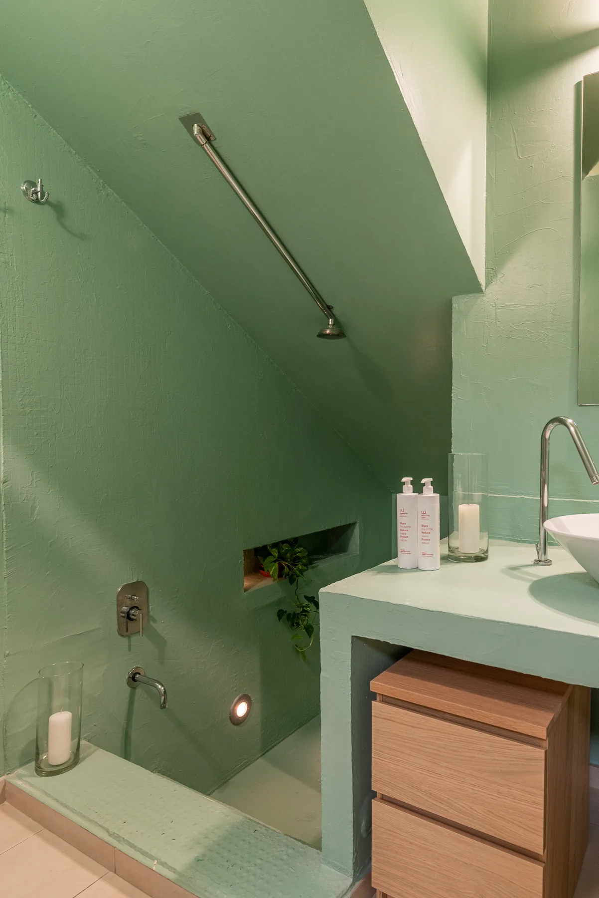 Un baño con azulejos verdes, ducha y mueble con lavabo.