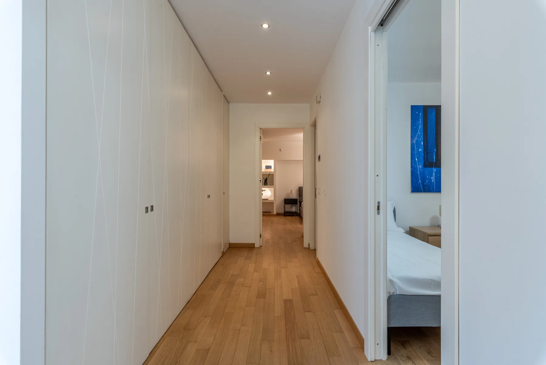 Un pasillo interior largo con suelo de madera y puertas a habitaciones contiguas.