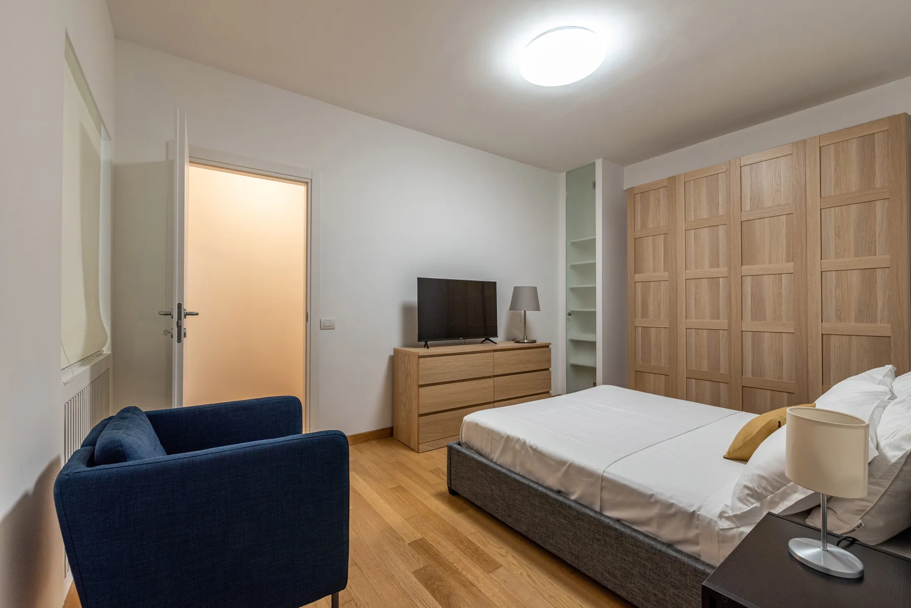 Un dormitorio con cama, armario de madera, cómoda y asientos azules.
