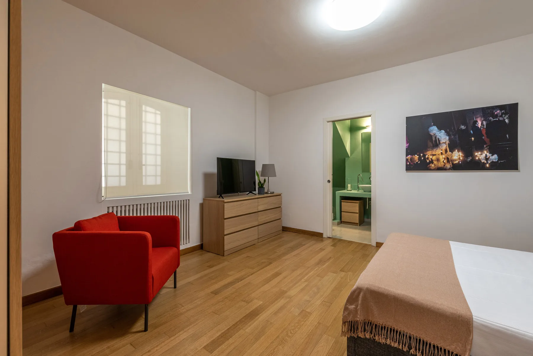 Un dormitorio con un sillón rojo, una cómoda y una puerta abierta al baño.