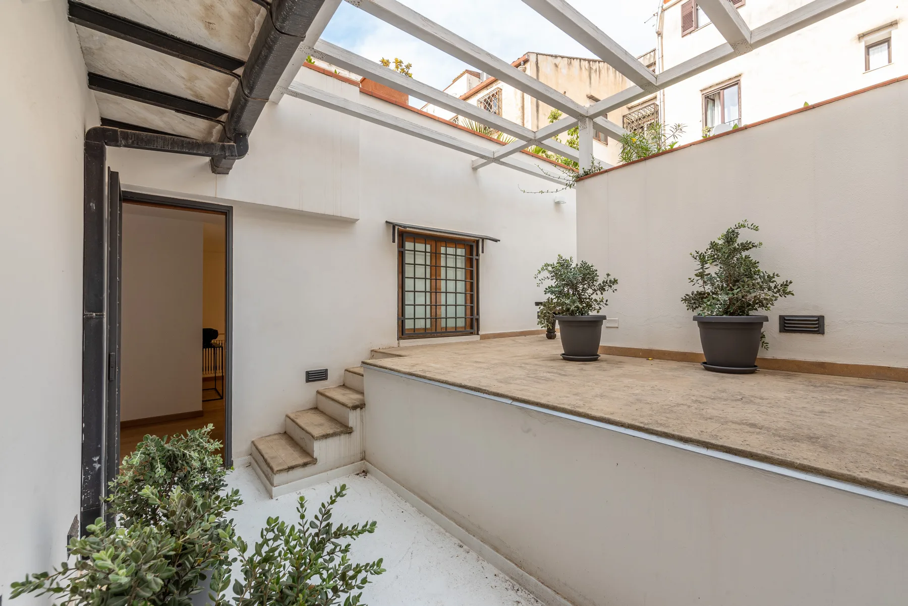 Un patio abierto con plantas en macetas y unos pequeños escalones.