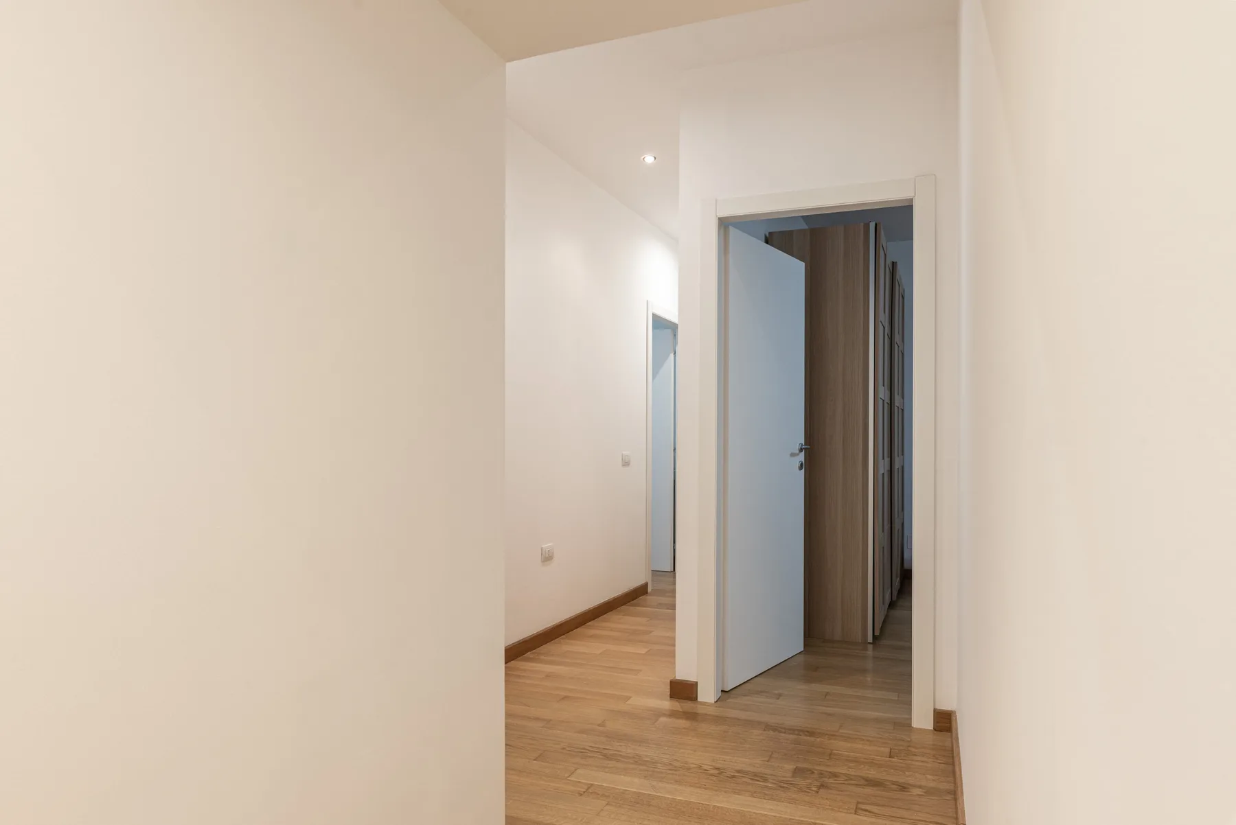 Un pasillo interior luminoso con suelo de madera y una puerta abierta.