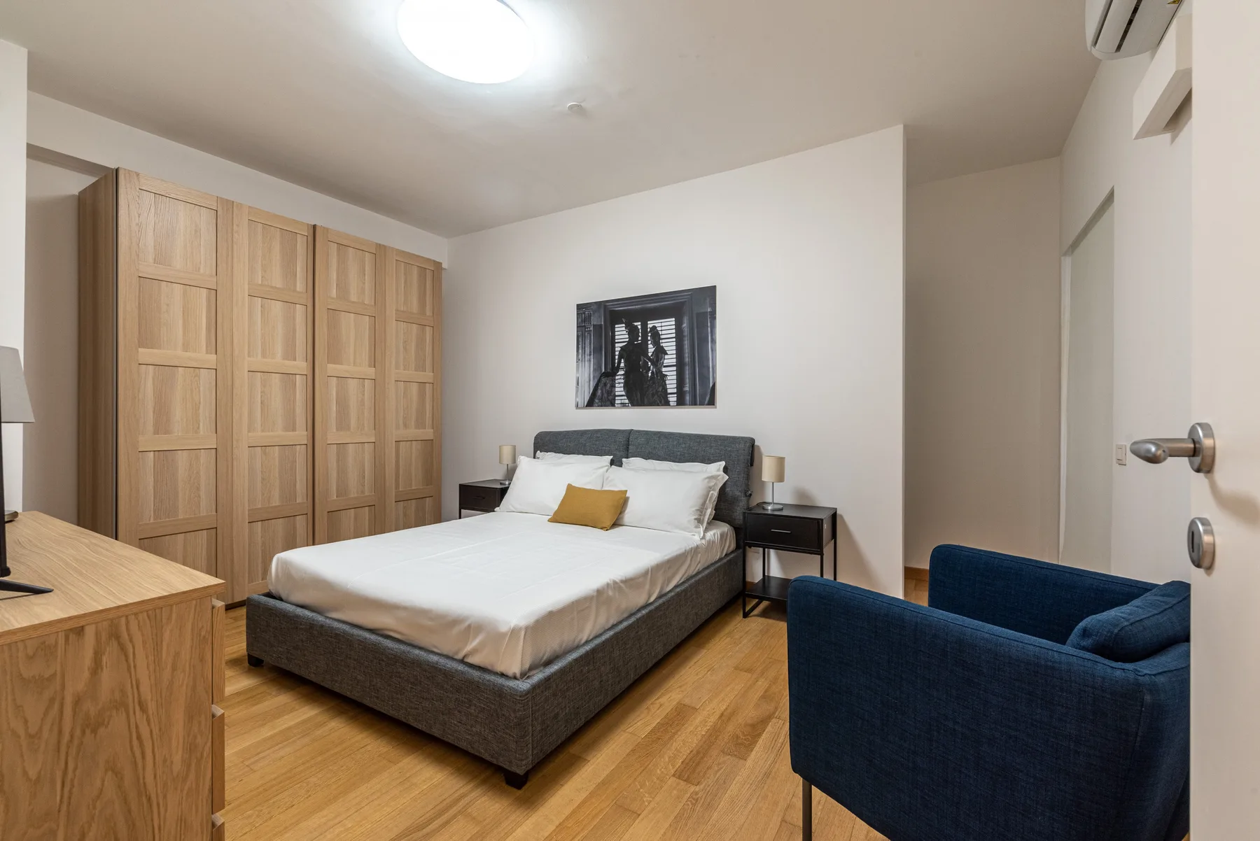 Un dormitorio con una cama, armarios de madera y un sillón azul.