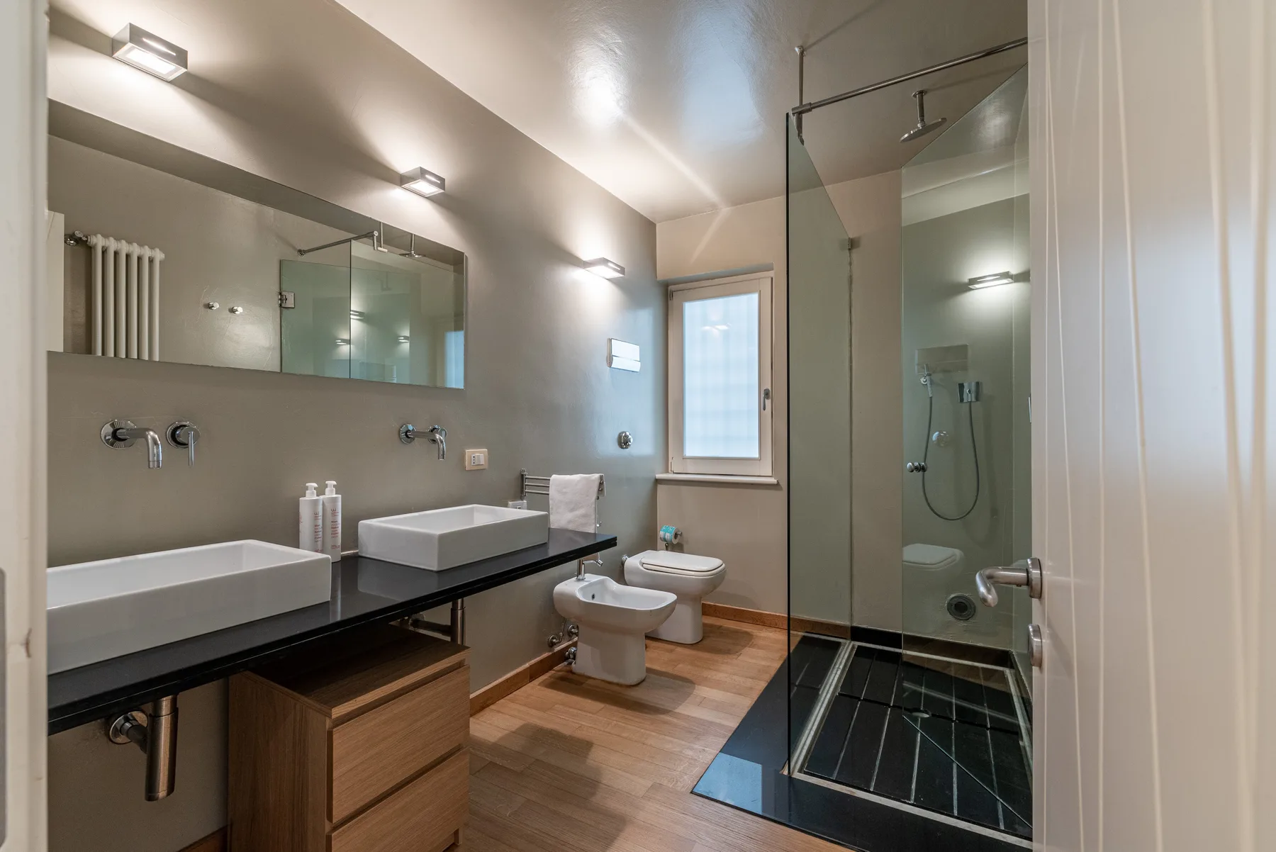Un baño moderno con un tocador largo y una ducha con mampara de vidrio.