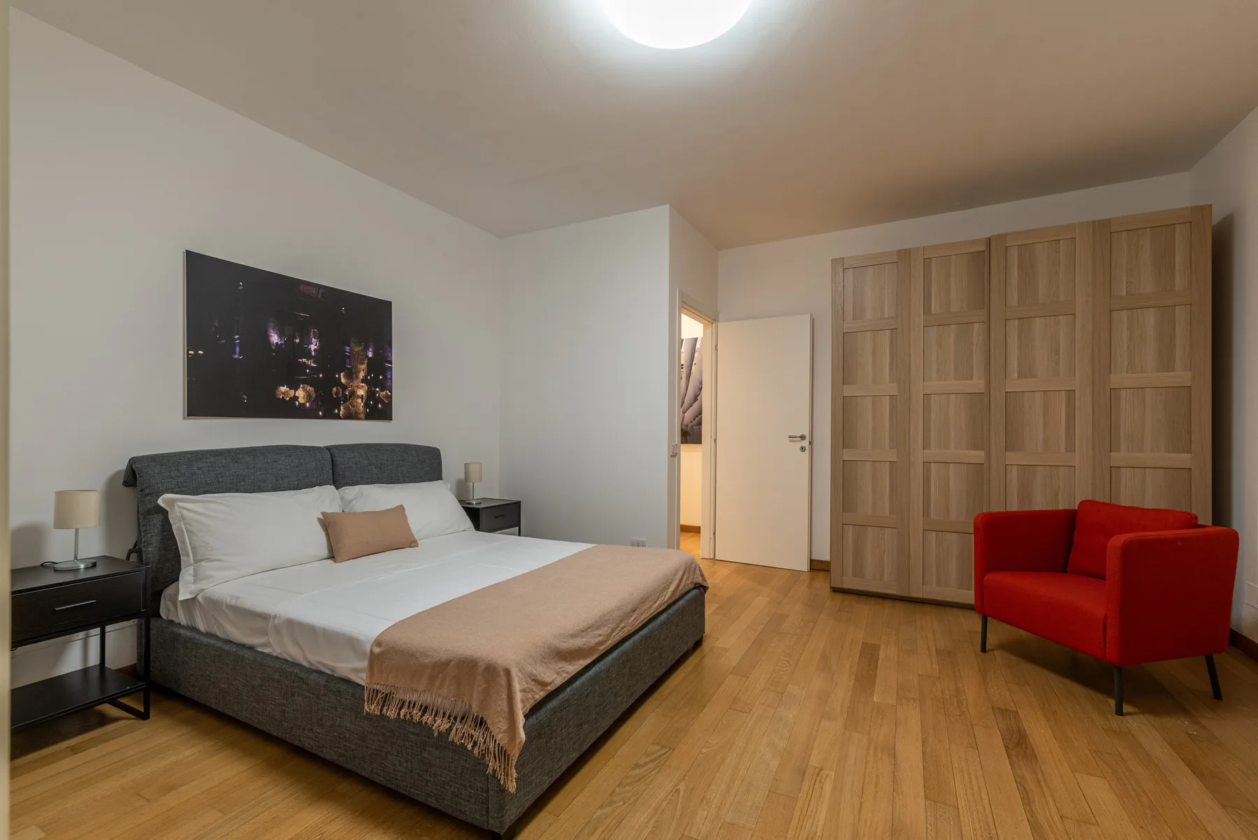 Un dormitorio con cama, armario de madera y sillón rojo.
