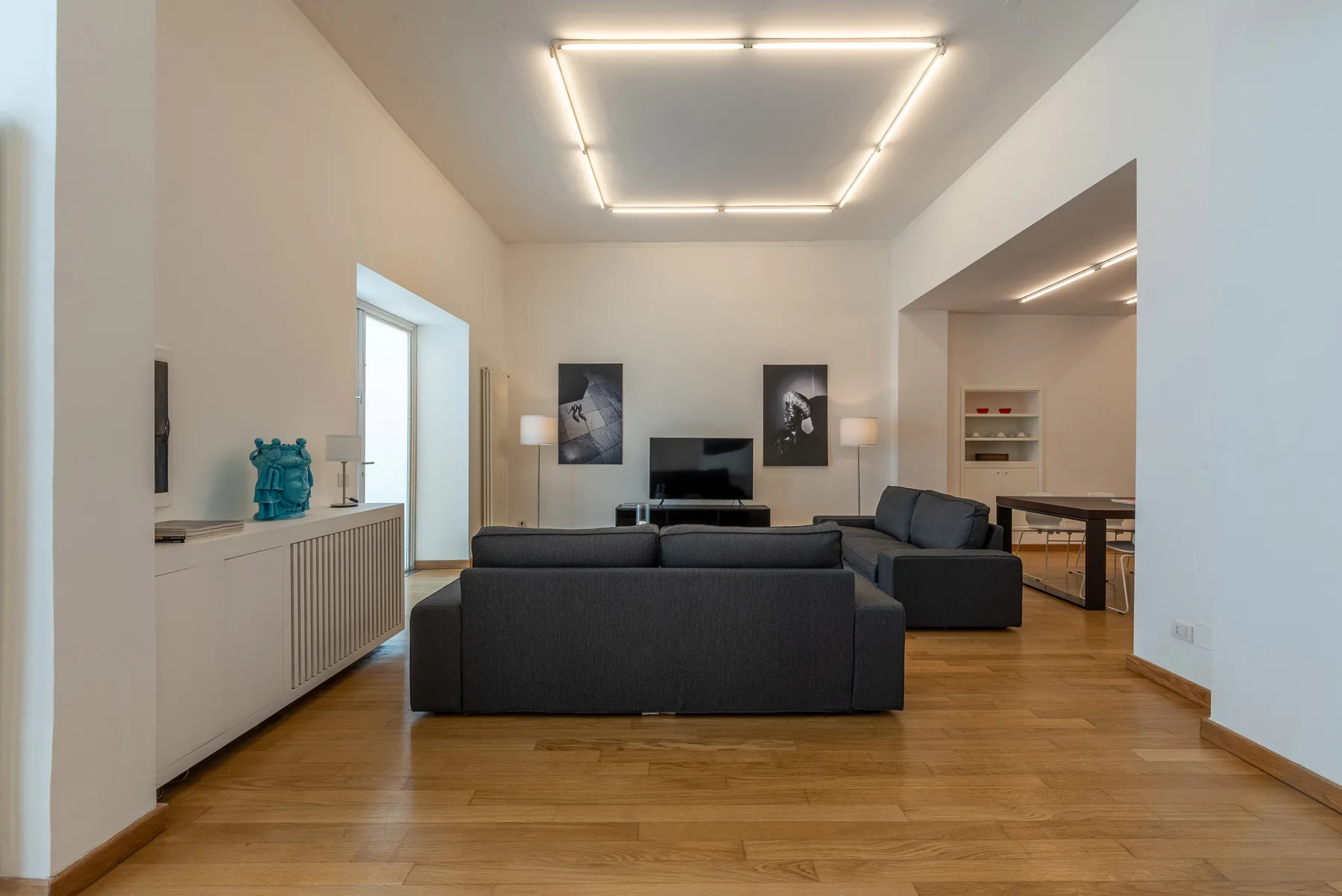 Una sala de estar moderna con asientos oscuros, un televisor y suelo de madera.