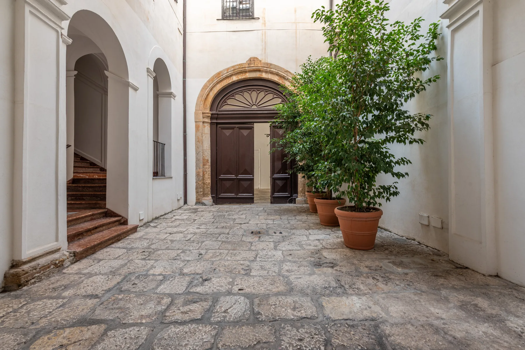 Un patio de piedra con una puerta de madera en arco y plantas en macetas.