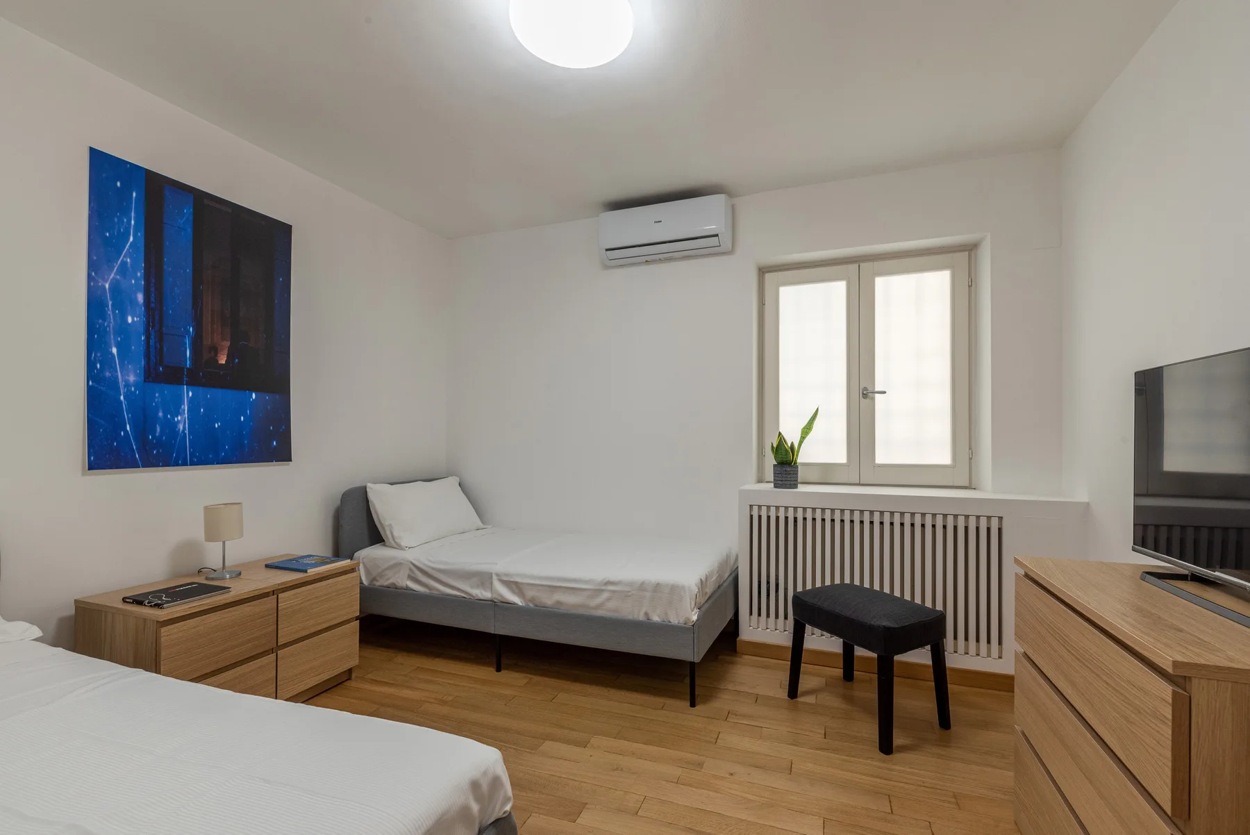 Un dormitorio con dos camas, una cómoda y una ventana con una planta en maceta.