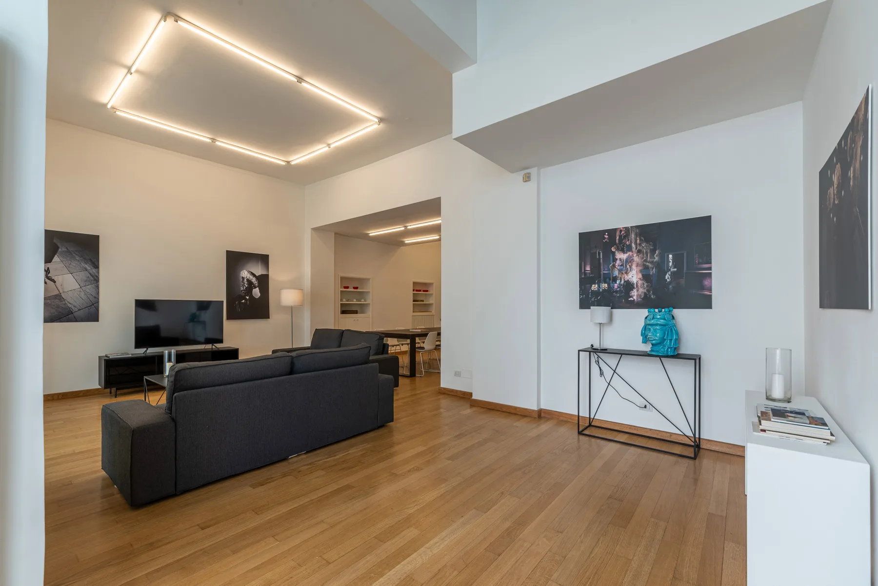 Una sala de estar moderna con asientos frente a un televisor y un comedor abierto.
