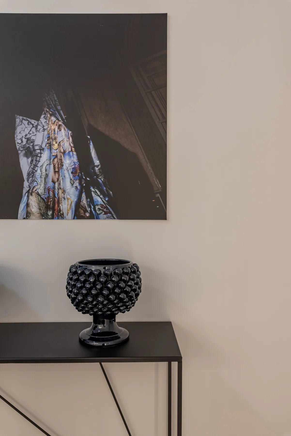 Una consola oscura está debajo de una obra abstracta, con un jarrón decorativo encima.