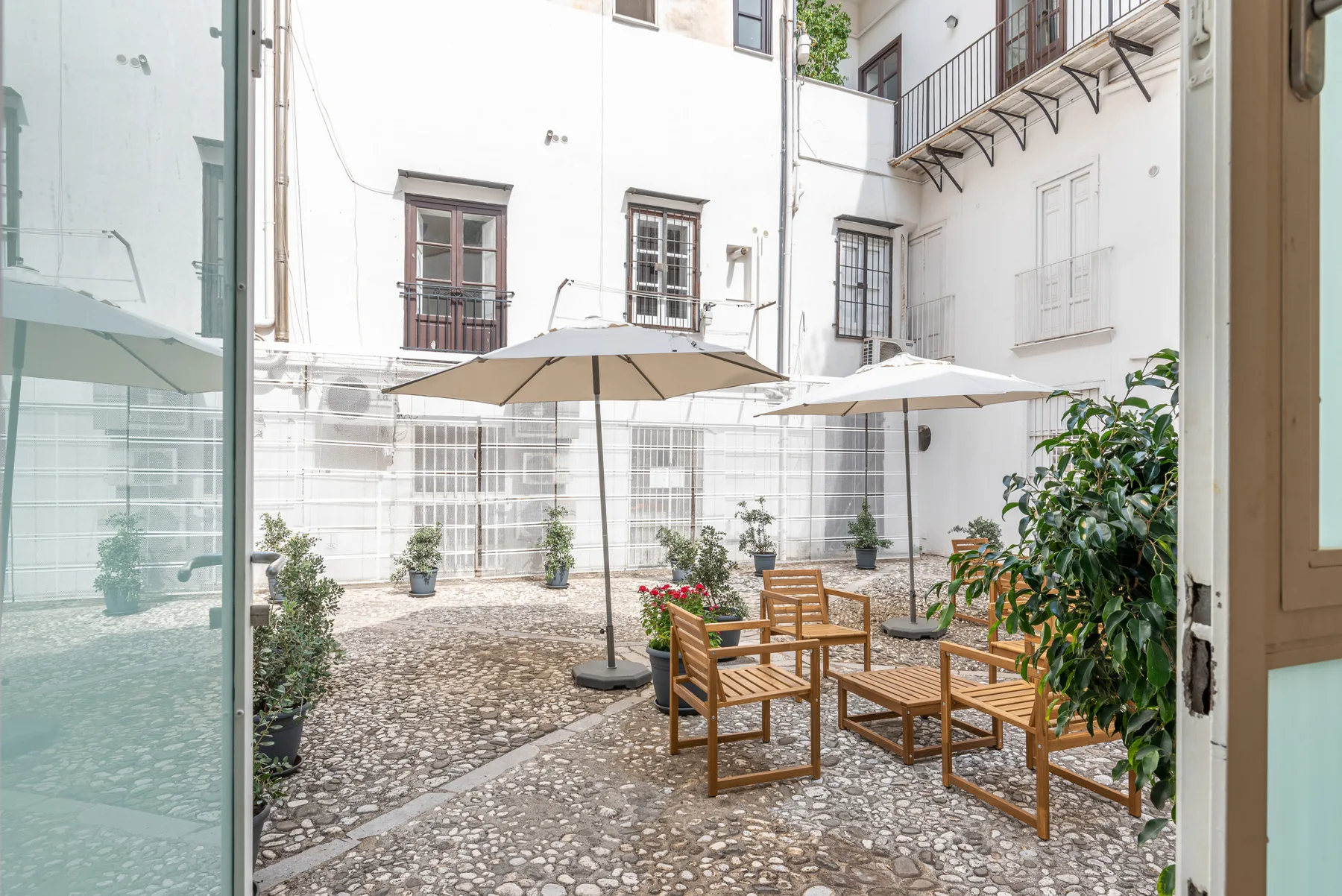 Un patio luminoso con asientos de madera, sombrillas y plantas en macetas.