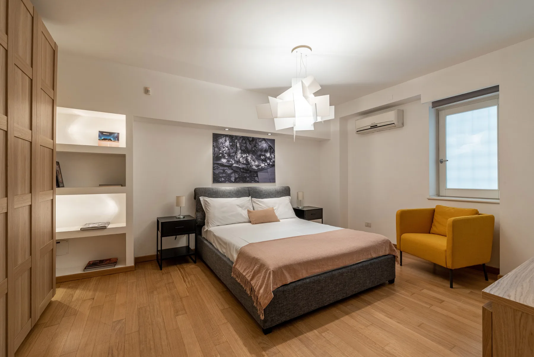 Un dormitorio con una cama, mesitas de noche y un sillón amarillo.