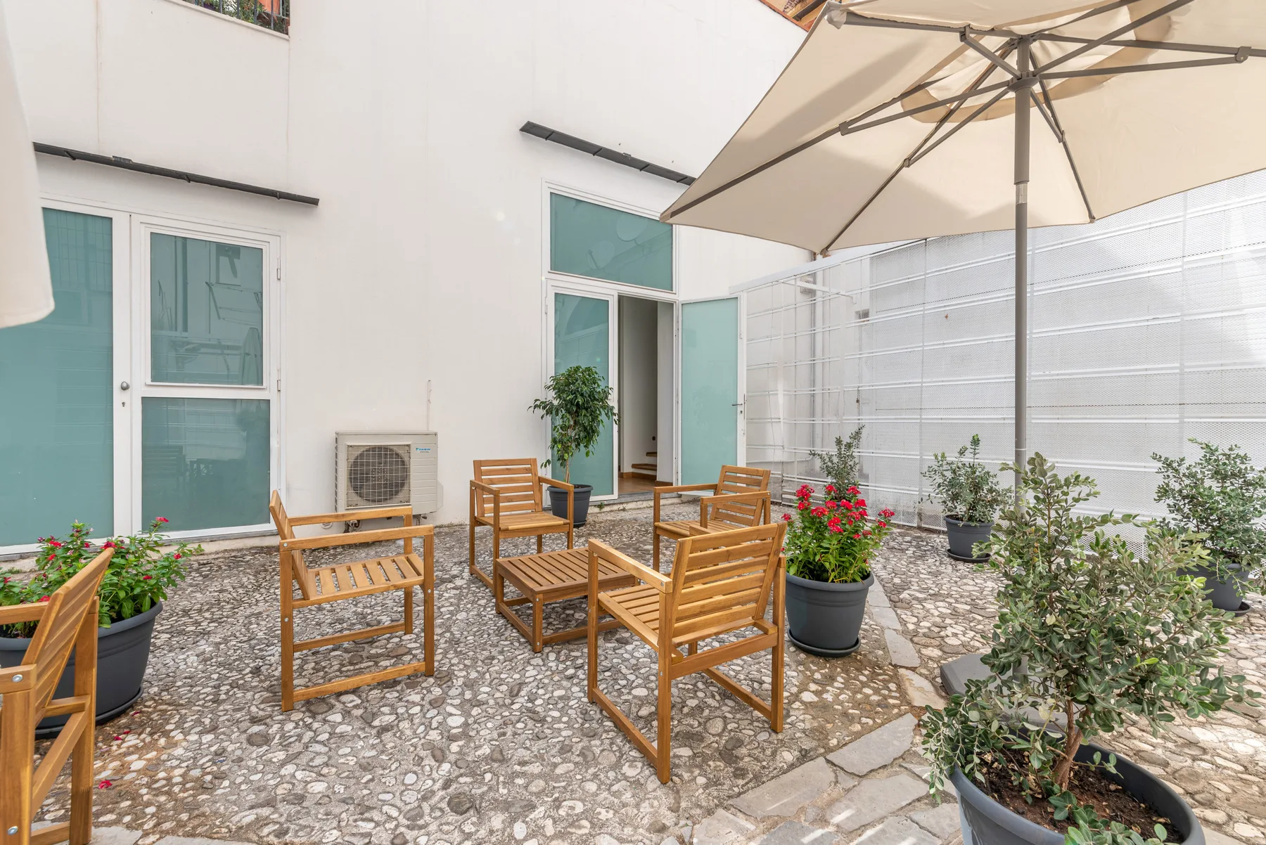 An outdoor patio with wooden seating, potted plants, and a large umbrella.