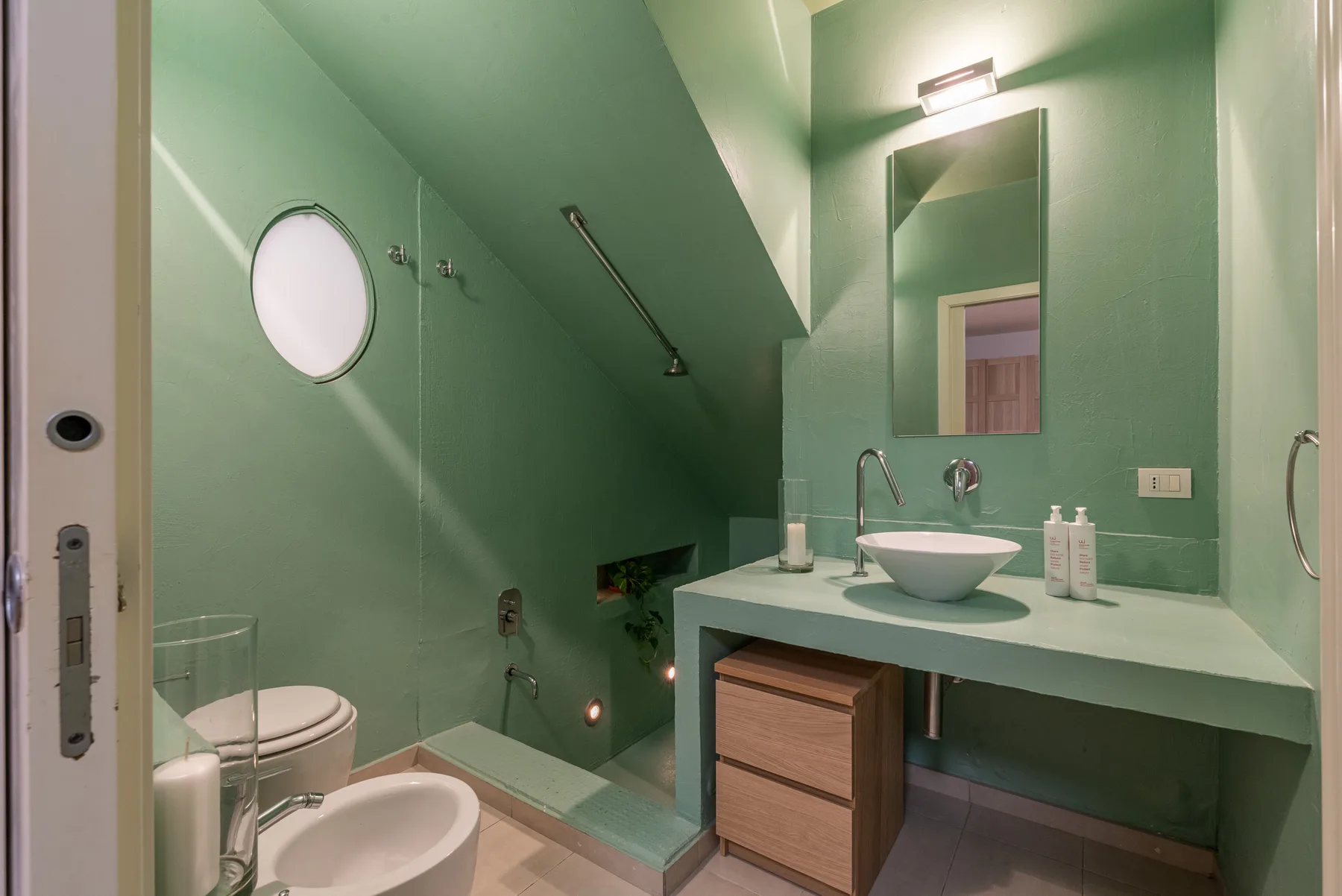 Un baño verde con lavabo, espejo y zona de ducha.